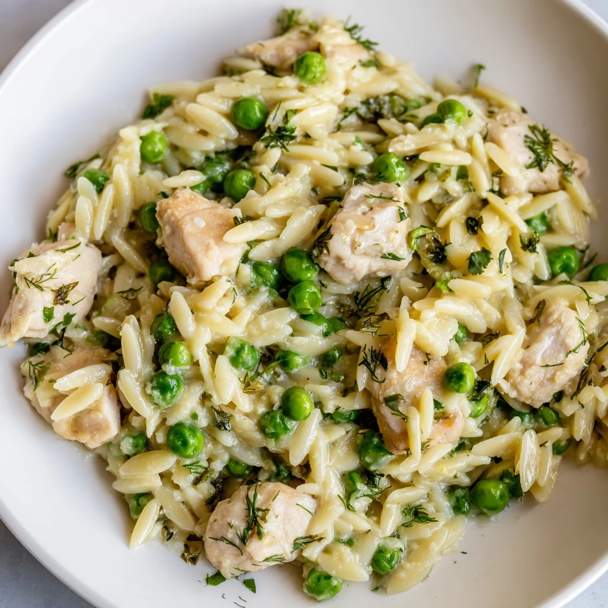 Colorful Mediterranean-inspired lemon herb chicken orzo skillet features juicy chicken, orzo, and peas in a tangy sauce, topped with fresh parsley and dill for serving.