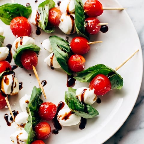 Fresh Caprese Salad Skewers glistening with balsamic glaze, layered with cherry tomatoes and mozzarella cheese.
