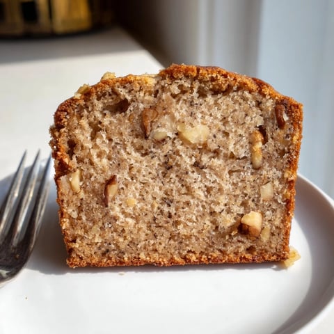 Warm Simple Banana Bread loaf, golden brown and gently sliced, ready to eat alongside coffee.