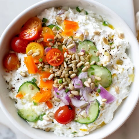 Creamy cottage cheese snack bowl with fresh veggies, herbs, and crunchy sunflower seeds topping.
