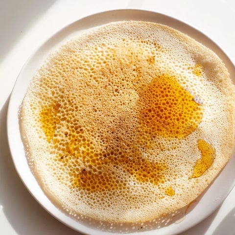 Golden-holed Moroccan Baghrir crepes are ready, warm, and inviting with honey and butter drizzled over.