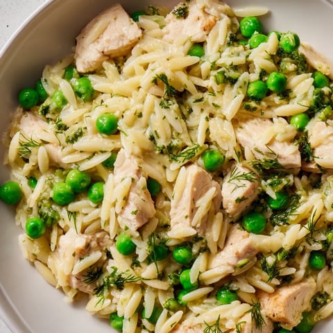 Tender golden chicken and vibrant green peas simmer in a zesty lemon sauce with orzo pasta, garnished with fresh herbs in this one-pan skillet.