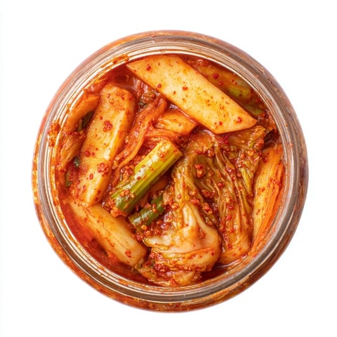 Vibrant homemade kimchi with bright red chili paste coating crunchy napa cabbage and julienned daikon in a glass jar, ready for fermentation.  