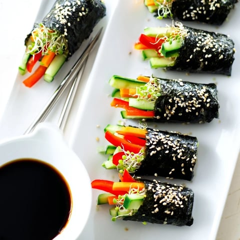Freshly rolled Nori Rolls with Vegetables featuring crisp cucumber, creamy avocado, and crunchy sprouts on a wooden board.  