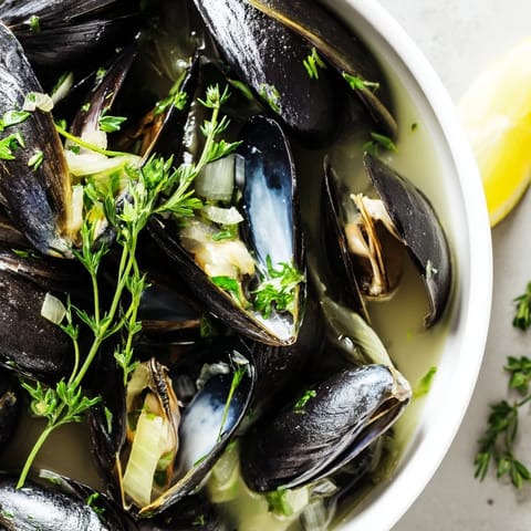 A close-up of delicious Belgian Moules Marinière, ready to be enjoyed with crusty bread and lemon wedges.