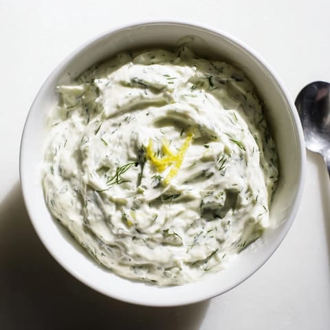 Freshly made Greek Yogurt Herb Dip in a white bowl, surrounded by colorful bell pepper strips and carrot sticks for a healthy snack.  