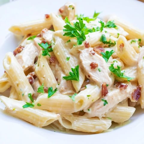 Close-up of Creamy Chicken Bacon Penne in a skillet, showcasing melted Parmesan sauce clinging to each penne noodle, with golden chicken and smoky bacon pieces.