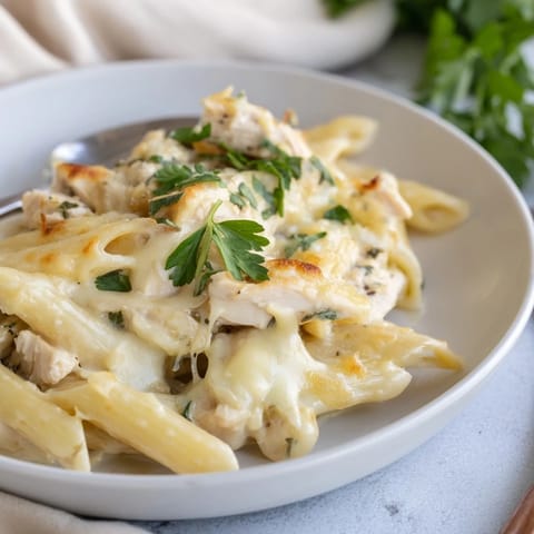 A serving of Chicken Alfredo Casserole on a white plate, garnished with fresh parsley.