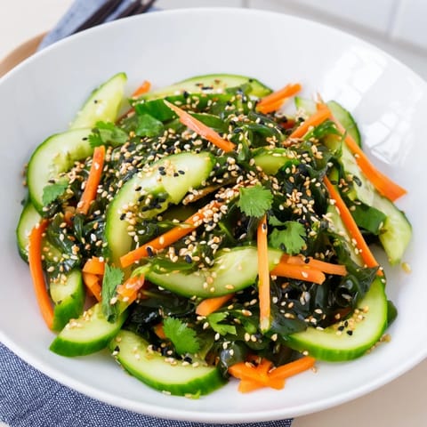 A vibrant bowl of Seaweed Salad with crisp cucumber, julienned carrot, and rehydrated wakame, dressed in a tangy sesame-ginger vinaigrette.