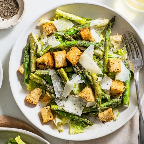Freshly shaved Parmesan and cracked black pepper garnish this vibrant Roasted Asparagus Caesar Salad, served on a rustic plate.
