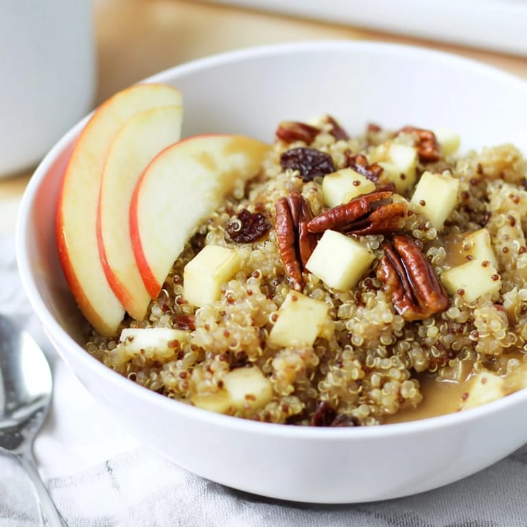 A comforting close-up shot of a warm Apple Cinnamon Quinoa Bowl topped with chopped nuts and raisins.