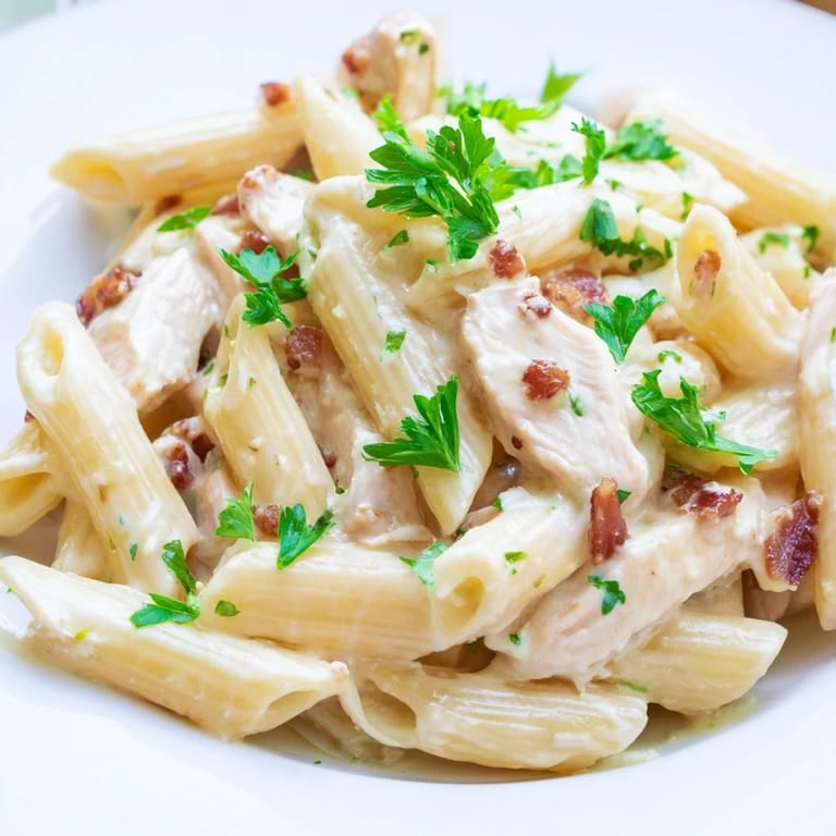 Close-up of Creamy Chicken Bacon Penne in a skillet, showcasing melted Parmesan sauce clinging to each penne noodle, with golden chicken and smoky bacon pieces.