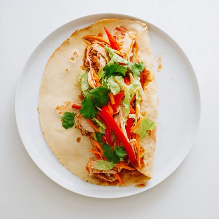 A close-up view of the Honey Sriracha Chicken Wrap with julienned carrots, red bell pepper, and fresh cilantro garnish on a rustic plate.