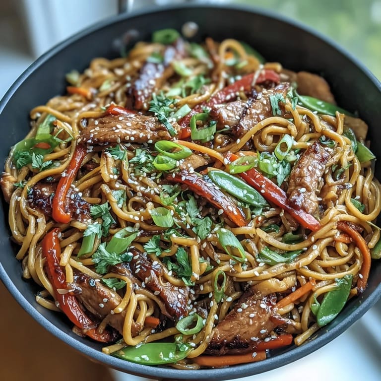 Serve this restaurant-style Pork Noodle Stir-Fry steaming and garnished with sesame seeds and cilantro for a satisfying family meal.