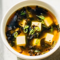 Bowl of steaming Japanese Wakame Soup with soft tofu cubes and fresh scallions.