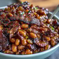 Hearty summer baked beans with crispy bacon, sweet brown sugar, and smoky paprika in a bubbling casserole.