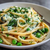 Creamy lemon pasta with peas and spinach, bright citrus aroma and fresh green garnish.